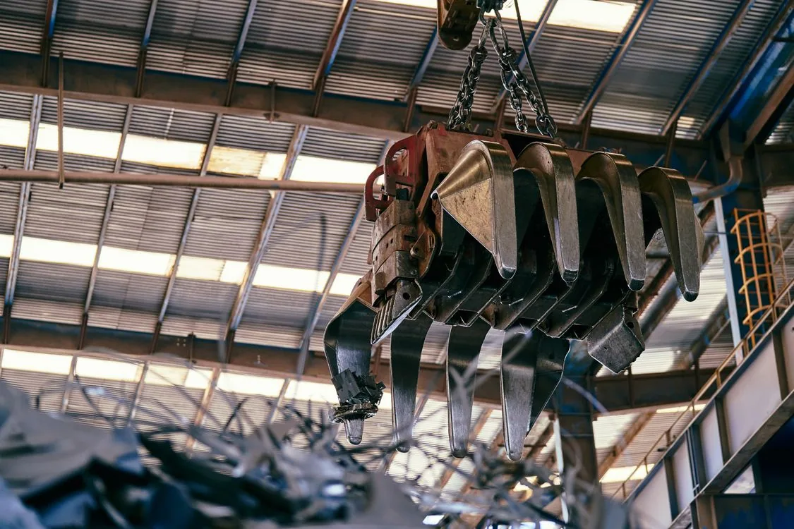 Crane handling scrap metal inside an industrial warehouse